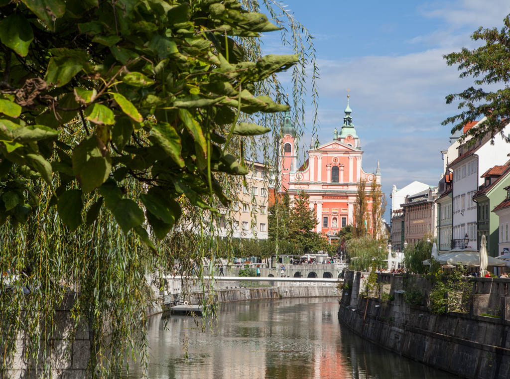View of a pink building along the river in Ljubljana, Slovenia with green foliage