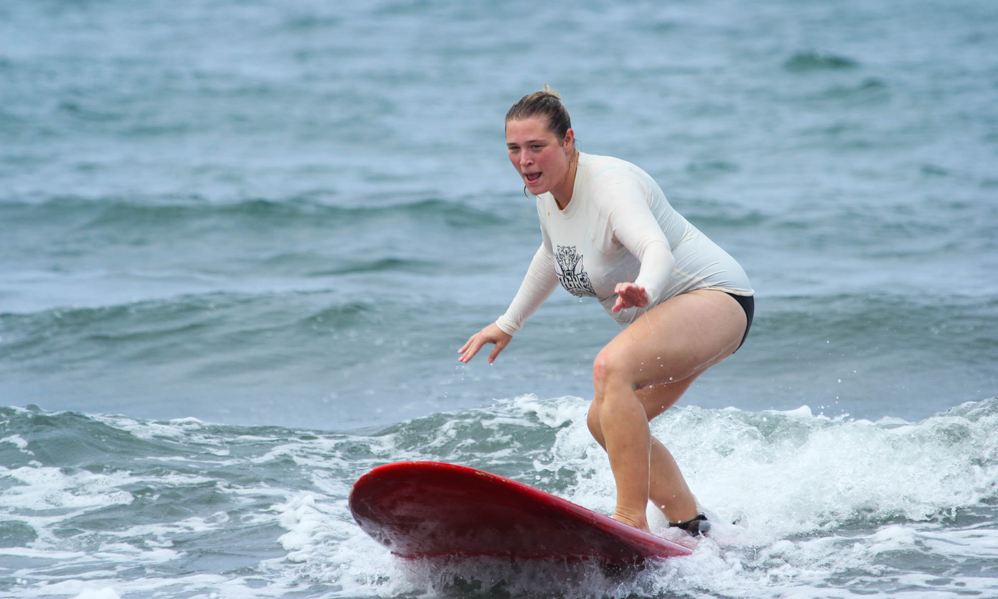 Woman in white shirt learning to surf on red surfboard