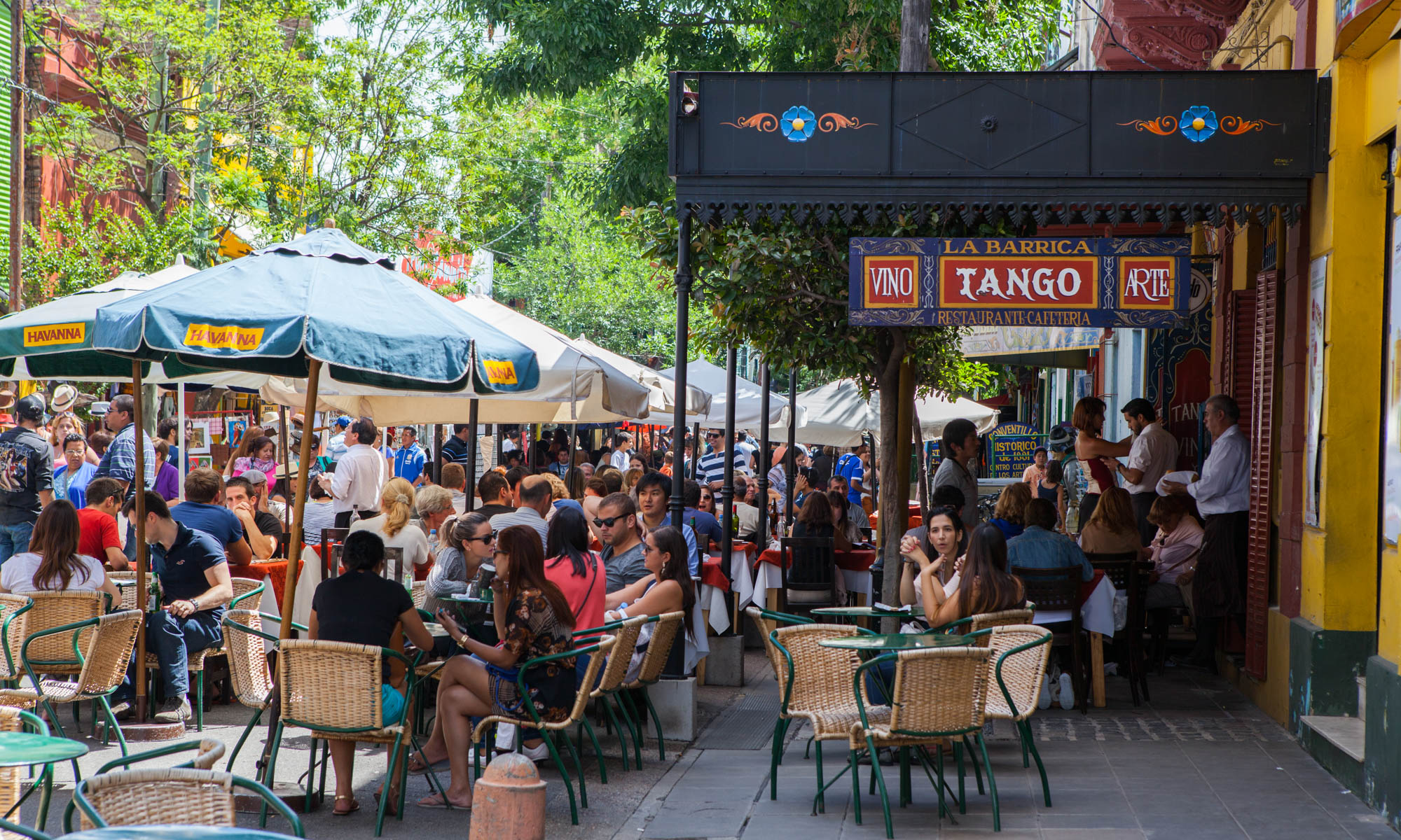 Busy street full of people and cafes in Buenos Aires with a Tango sign by the restaurant