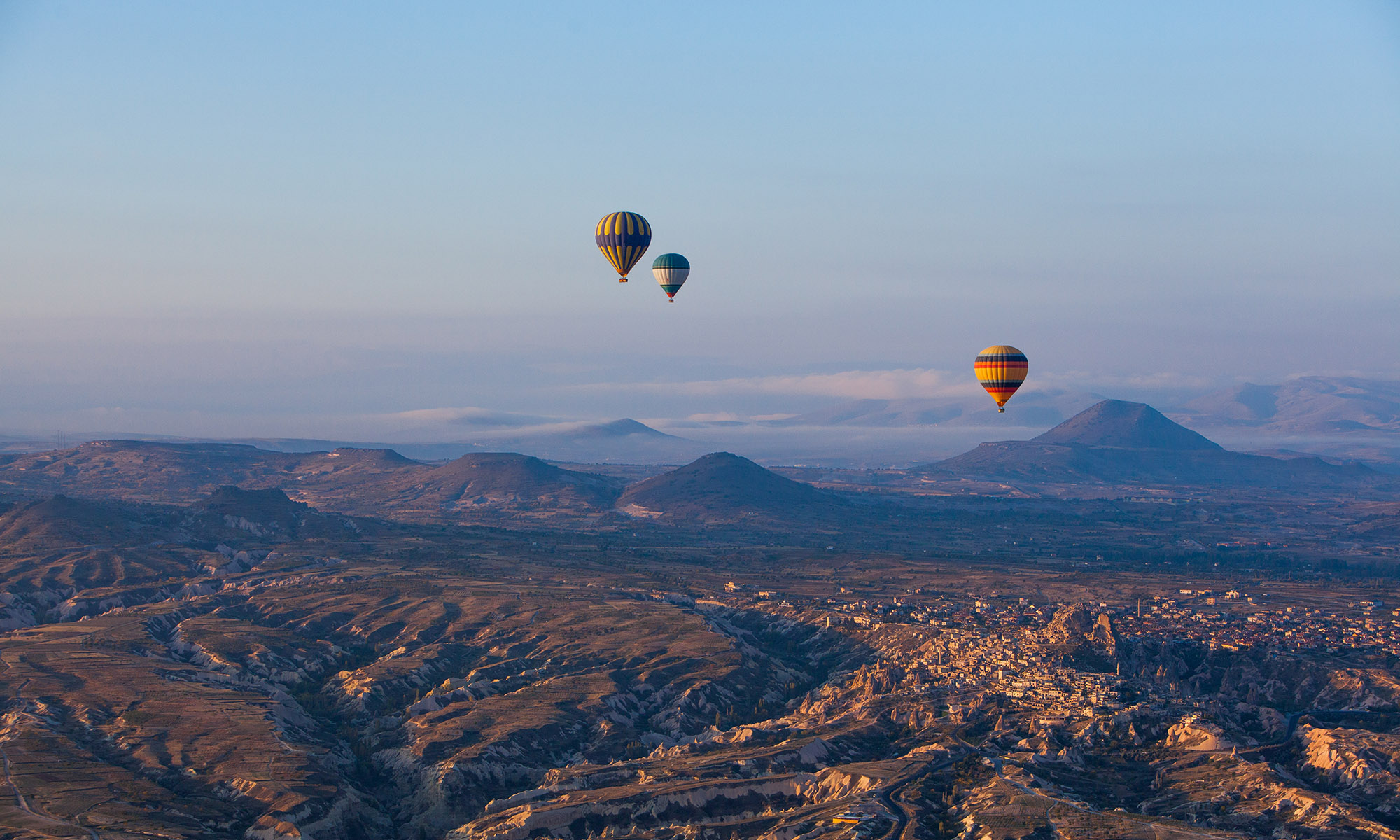 Three hot air balloons raising above the rough landscape of Cappadocia, Turkey at sunrise