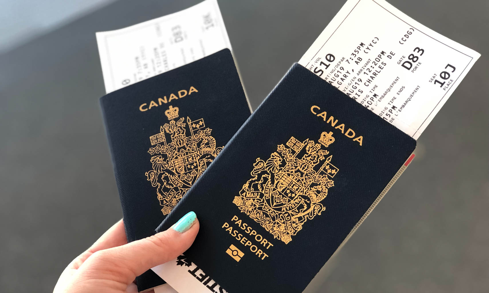 Close up of two Canadian passports being held by a person with blue nail polish