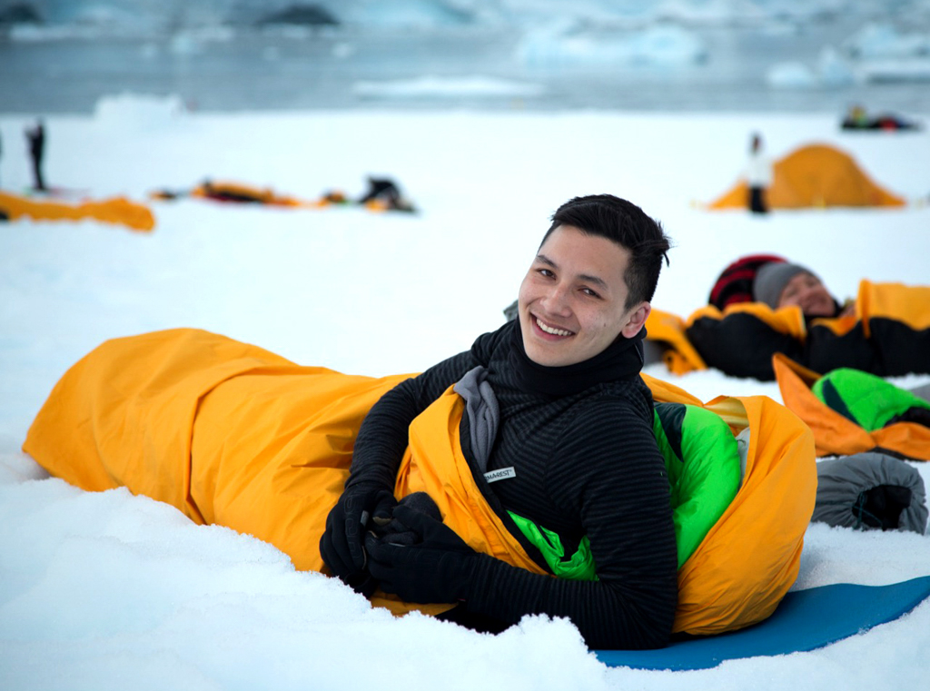 Smiling man in yellow sleeping bag on the snow in Antarctica