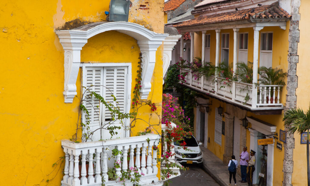street corner with historical yellow buildings and white terraces with red and pink flowers in the historic centre of Cartagena Colombia
