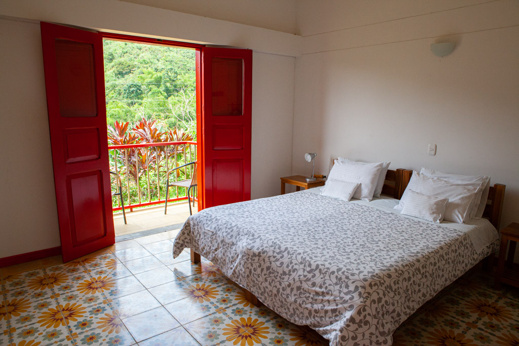 double bed in a room with red doors opening to a patio overlooking coffee fields